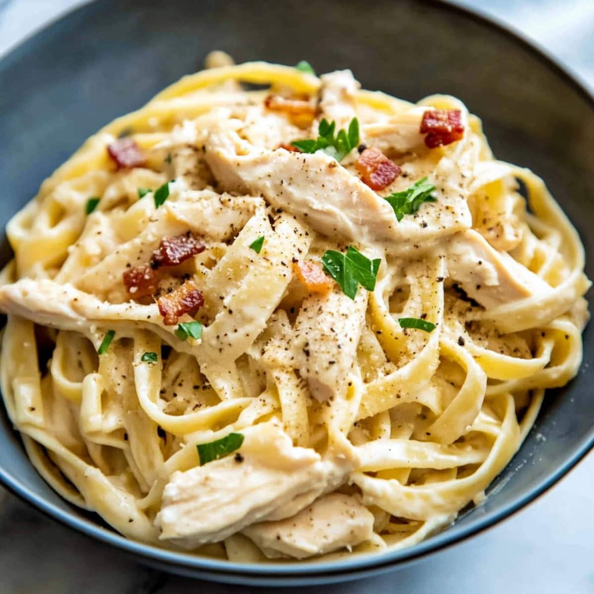 Loaded creamy chicken and bacon pasta in a black bowl with fresh herbs