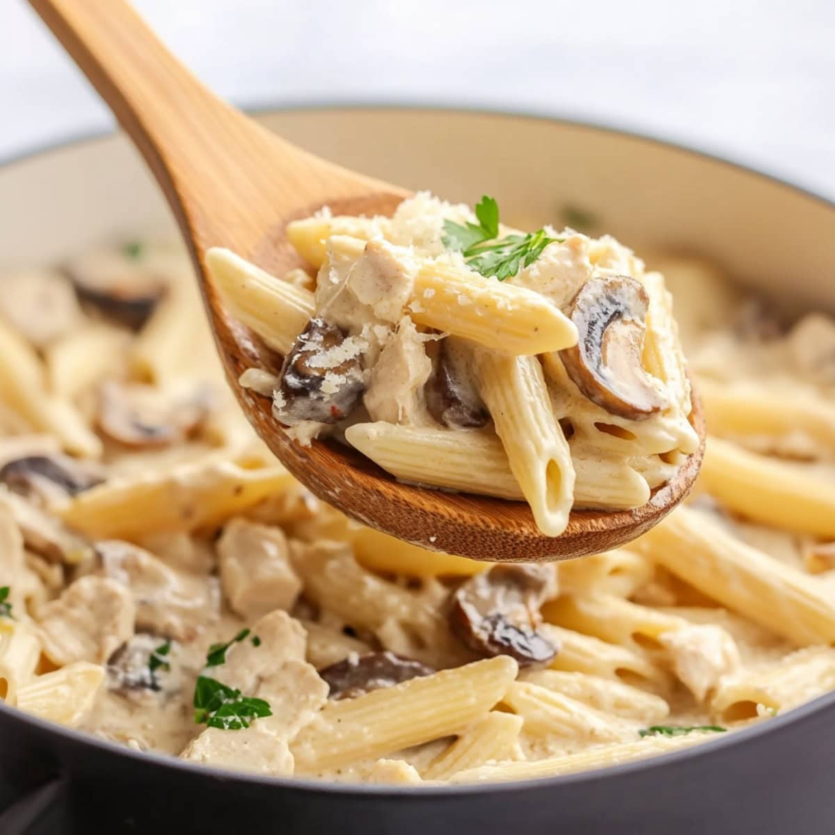 Wooden ladle lifting a serving of creamy chicken and mushroom pasta from a pan.