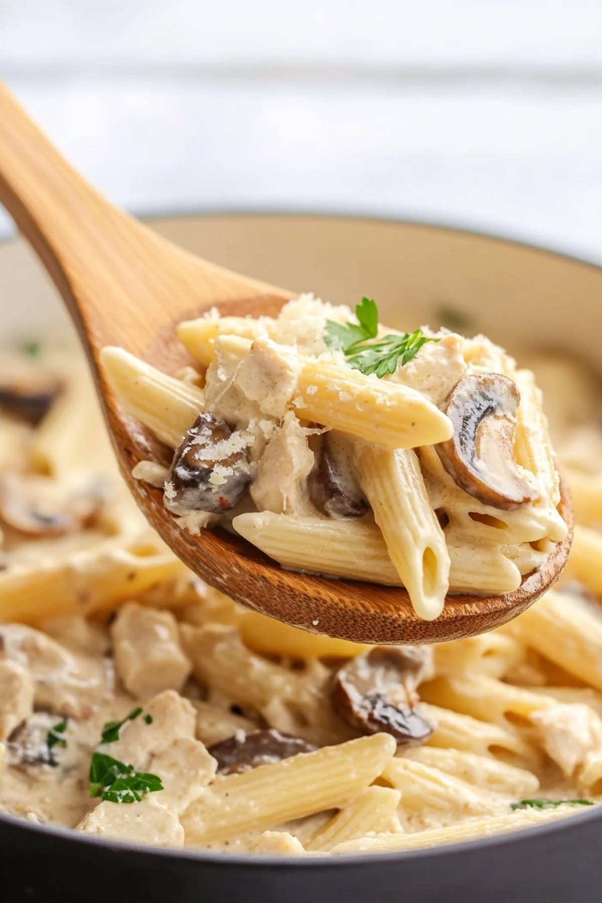 Creamy chicken and mushroom pasta scooped with a wooden ladle from skillet pan.