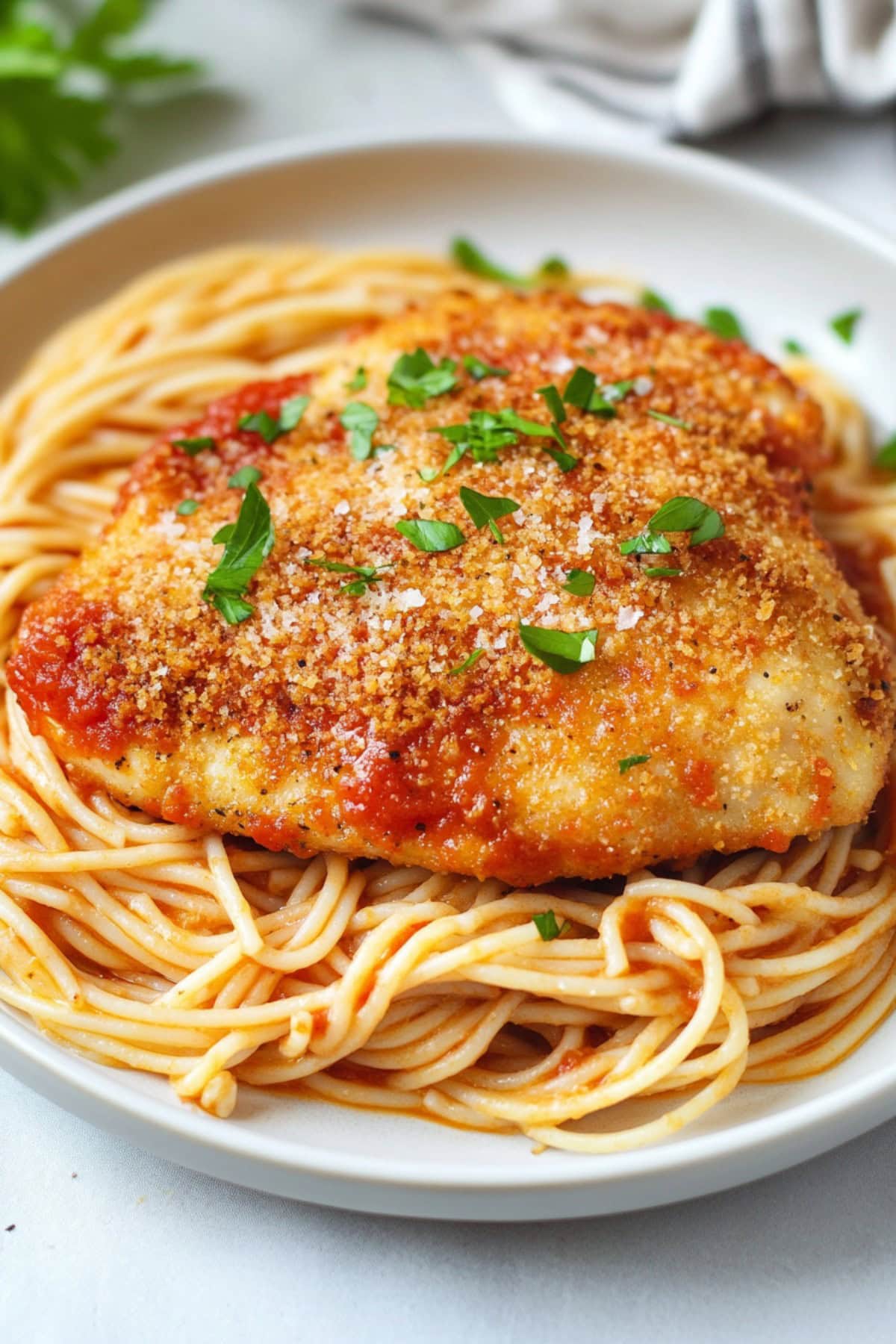 Crusted chicken Romano served with pasta in a white plate.