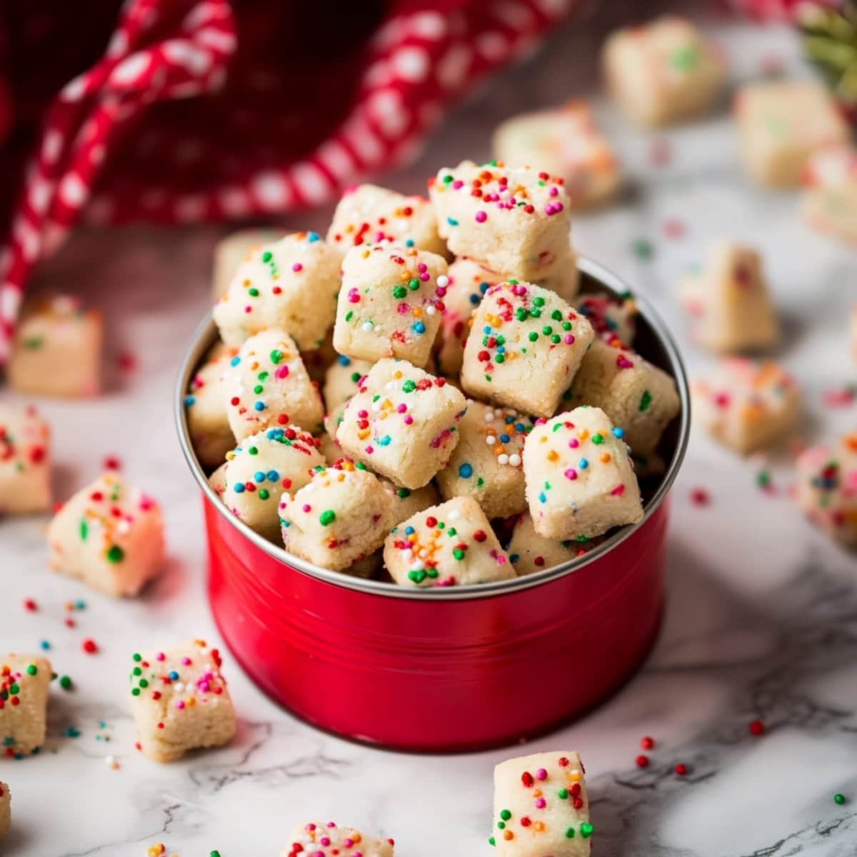 Funfetti shortbread bites in a festive red tin sitting on a white marble table.