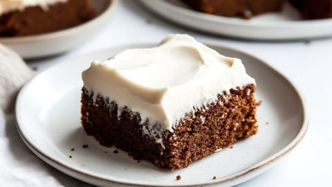 A plate of gingerbread sheet cake with creamy frosting at the top.