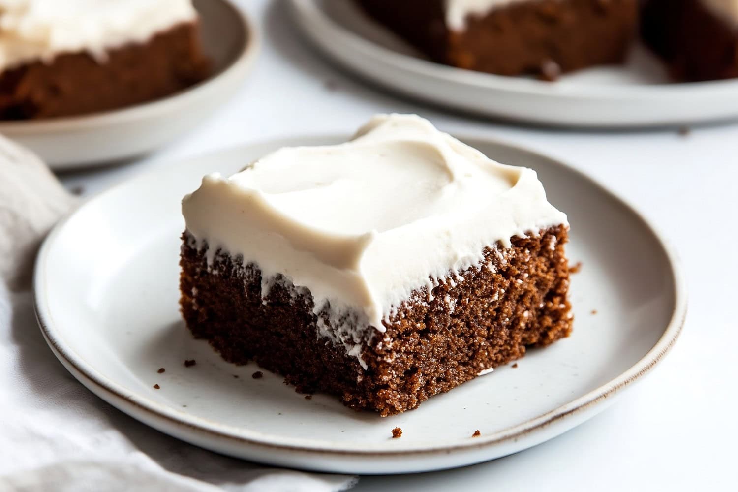 A plate of gingerbread sheet cake with creamy frosting at the top.