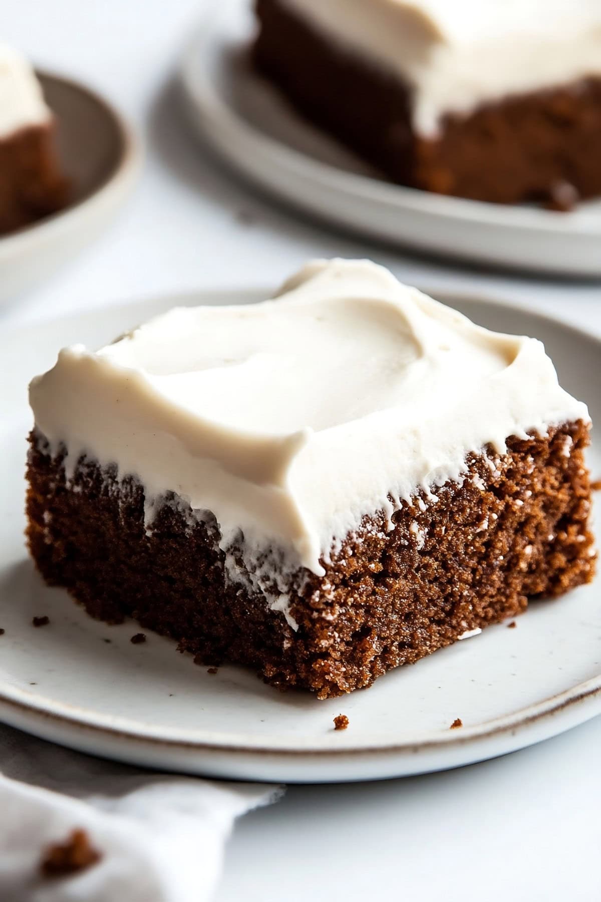 Slice of gingerbread sheet cake with cream cheese frosting on a plate