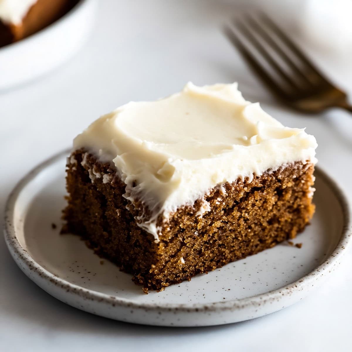 Spicy gingerbread sheet cake in a white plate on a white marble table.