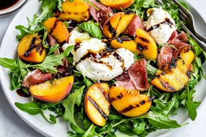 An elegant presentation of grilled peaches and burrata salad, with balsamic glaze artfully drizzled around the plate.