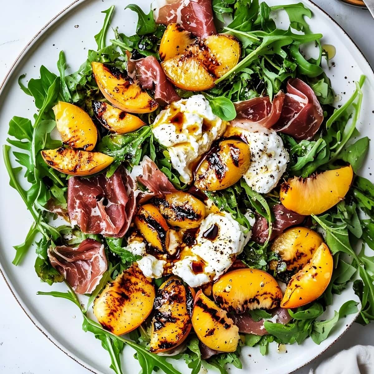 Homemade grilled peach and burrata salad with fresh greens and prosciutto.