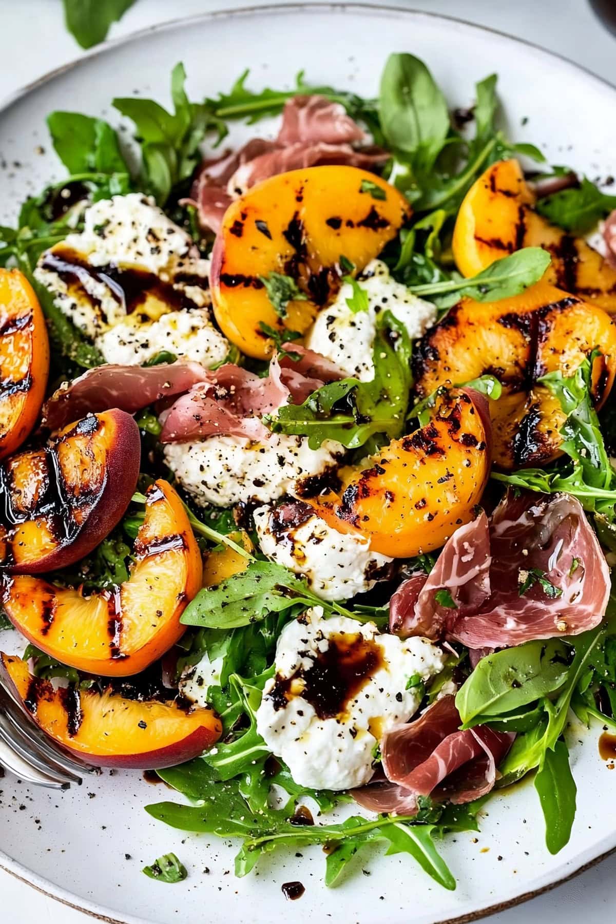 A colorful summer salad featuring grilled peaches, creamy burrata and a handful of mixed greens.