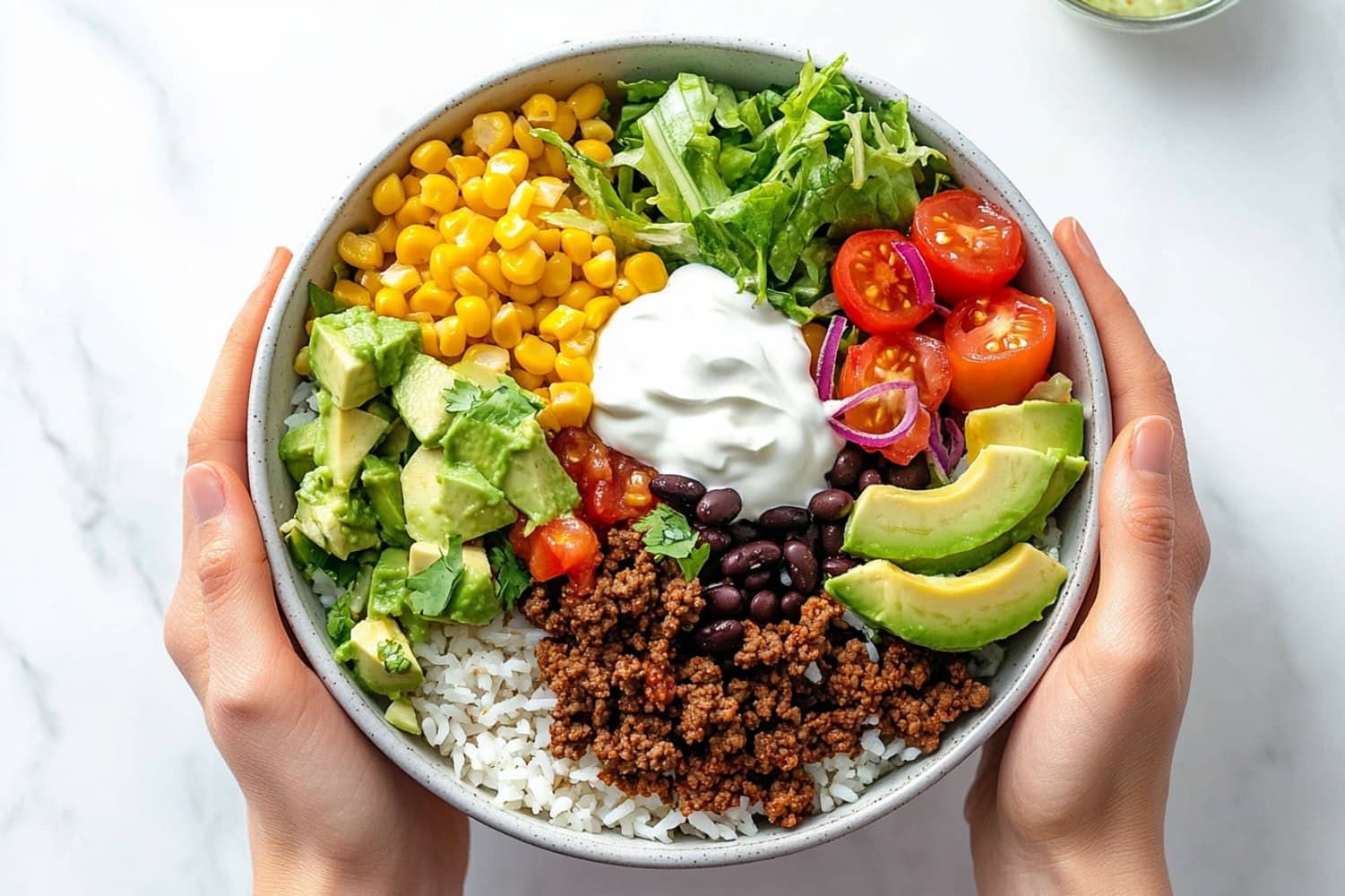 Cilantro lime rice in a white bowl topped with ground beef, black beans, corn and avocado.