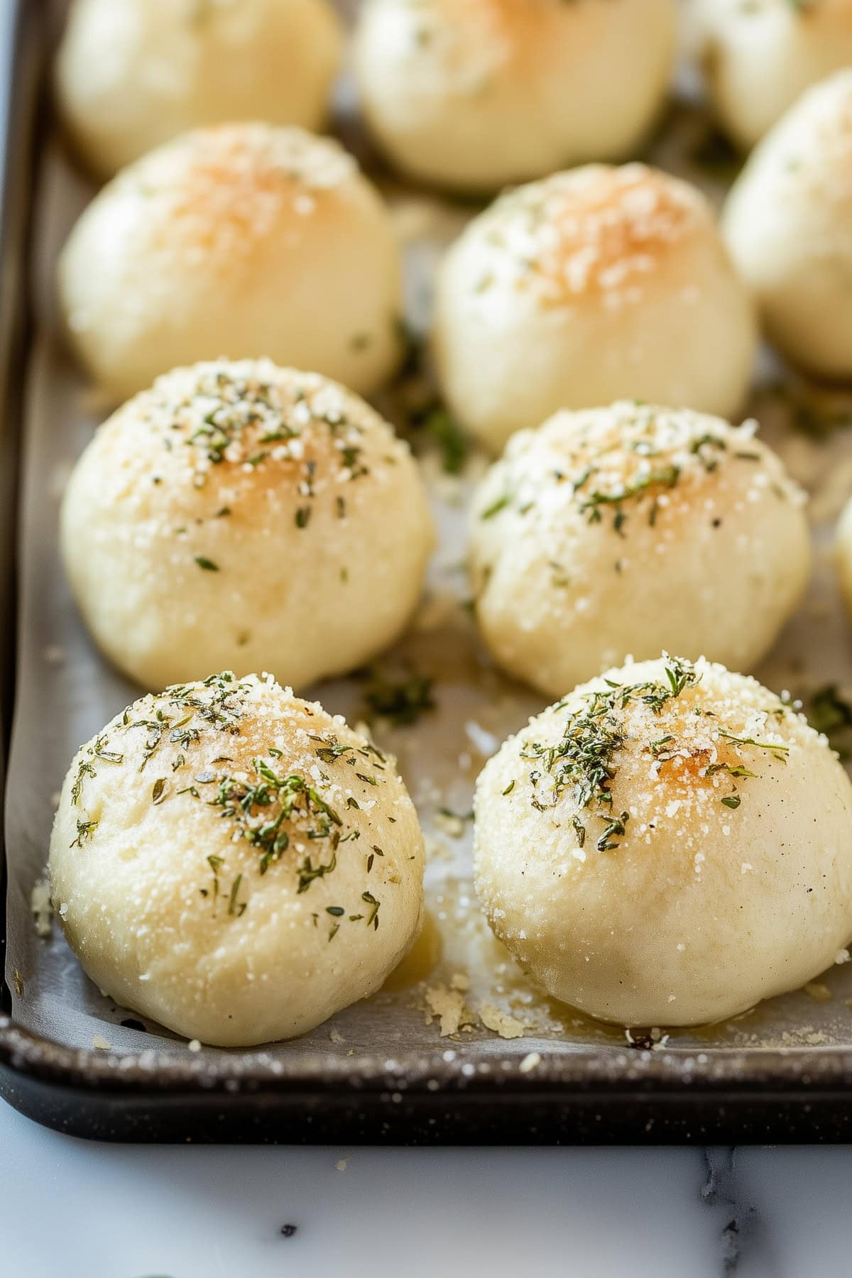 Biscuit cheese bombs on a baking tray topped with parmesan cheese and herbs