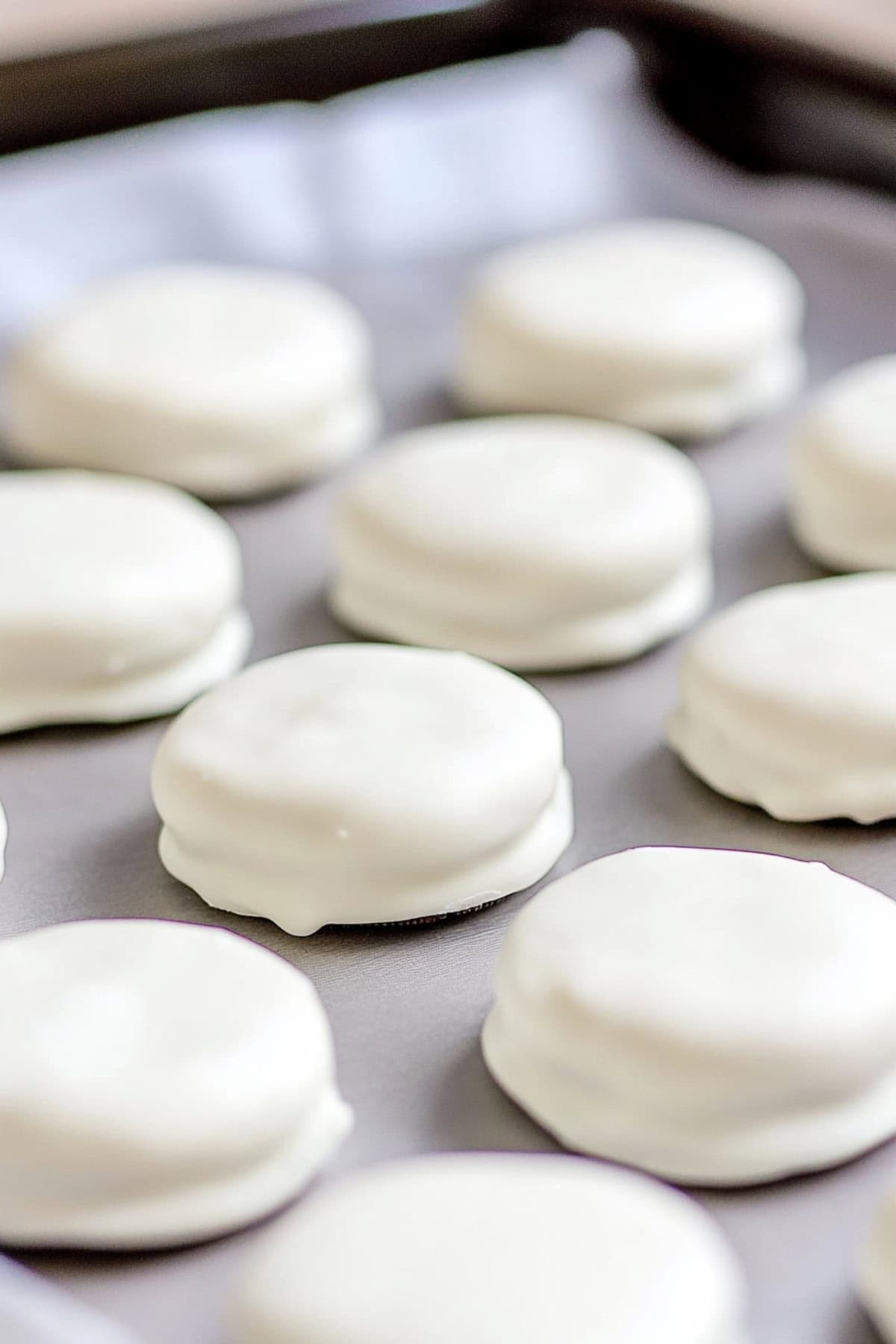 White chocolate covered Oreo cookies on a parchment lined baking sheet, close up.