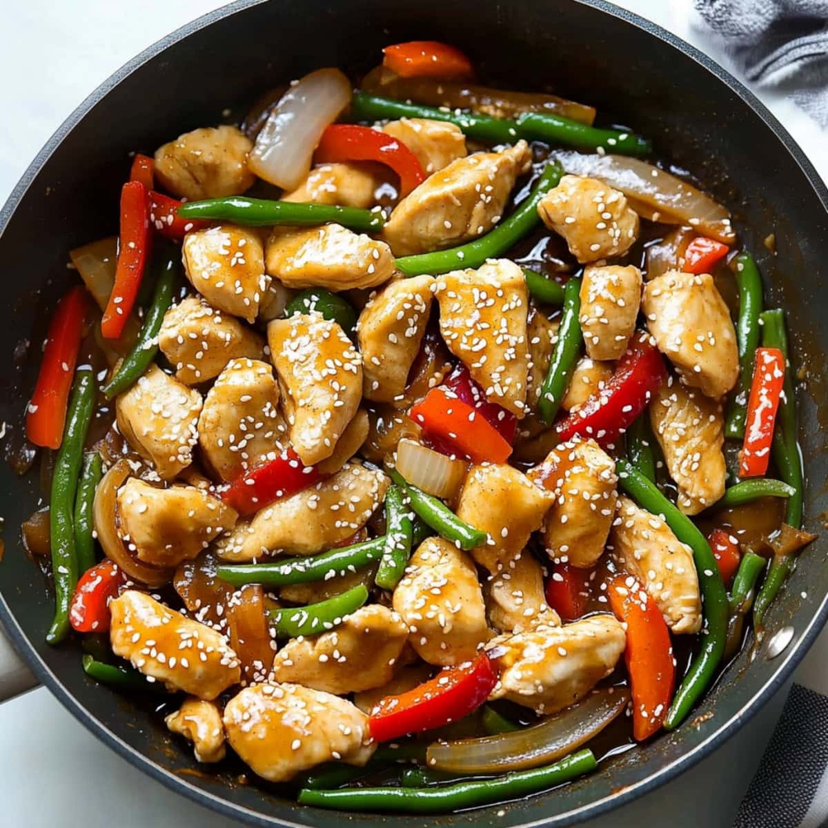 An overhead view of lemon chicken stir-fry with onions, green beans and red bell peppers.