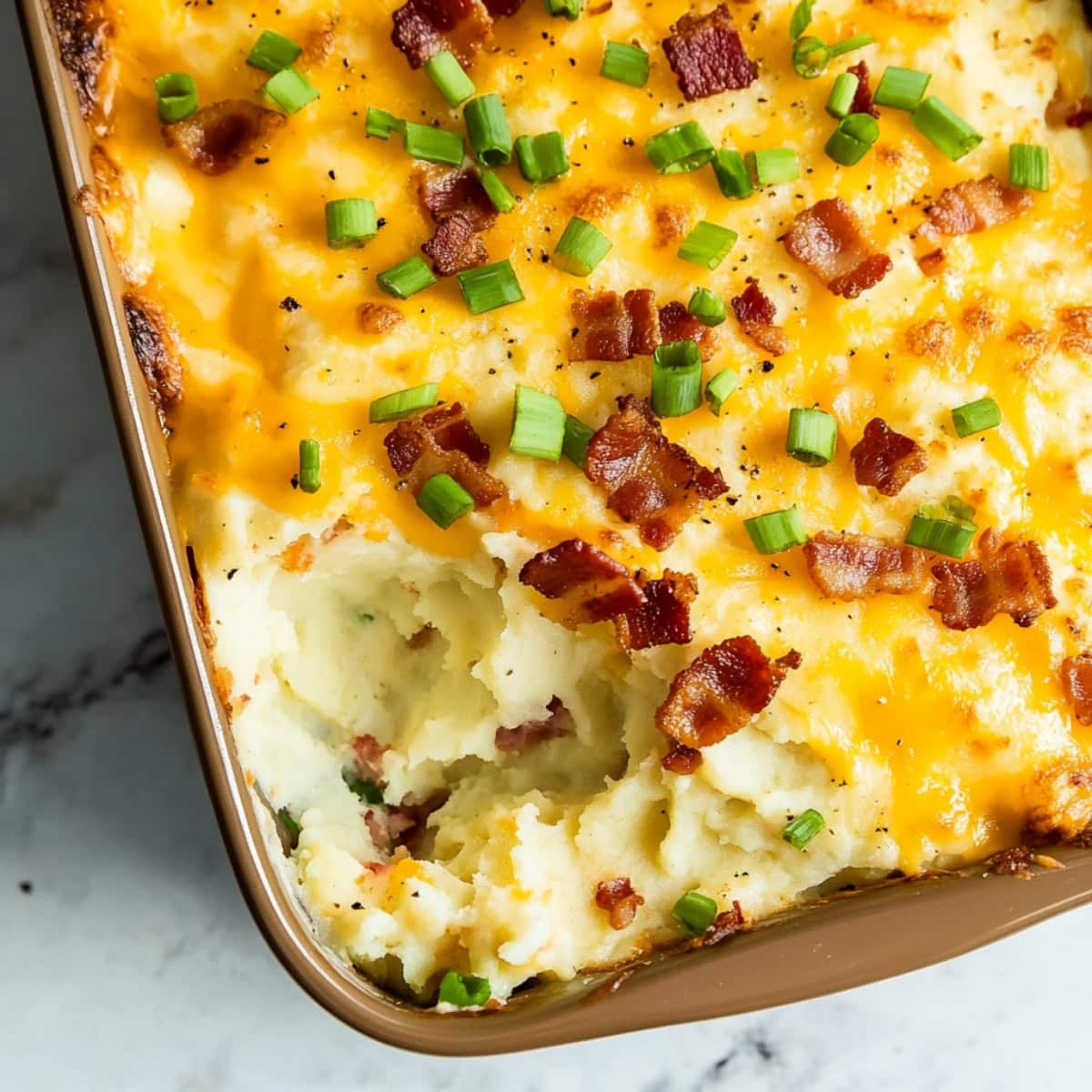 A casserole dish filled with loaded baked potatoes topped with cheddar and bacon.