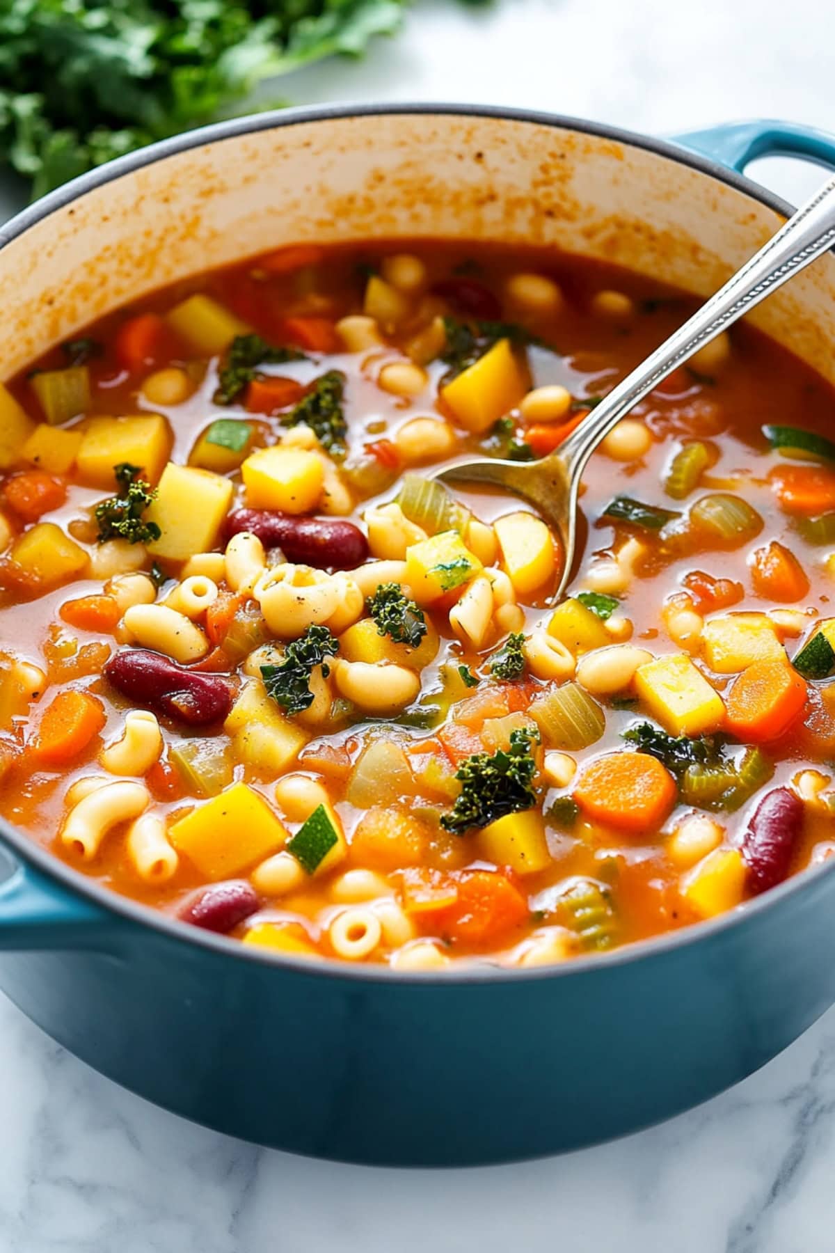 Colorful veggies, hearty beans, and tender pasta in a tomato-based broth cooked in a blue pot.  
