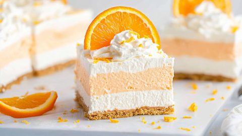 A tray of orange creamsicle dream bars, each square perfectly cut to display the orange and vanilla layers.