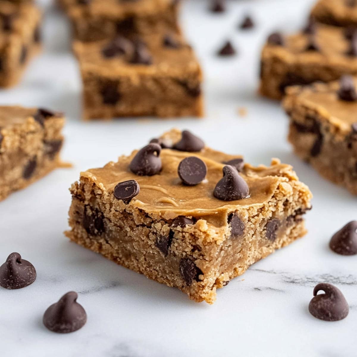 A close-up shot of golden-brown peanut butter chocolate chip bars cut into squares and stacked on a table