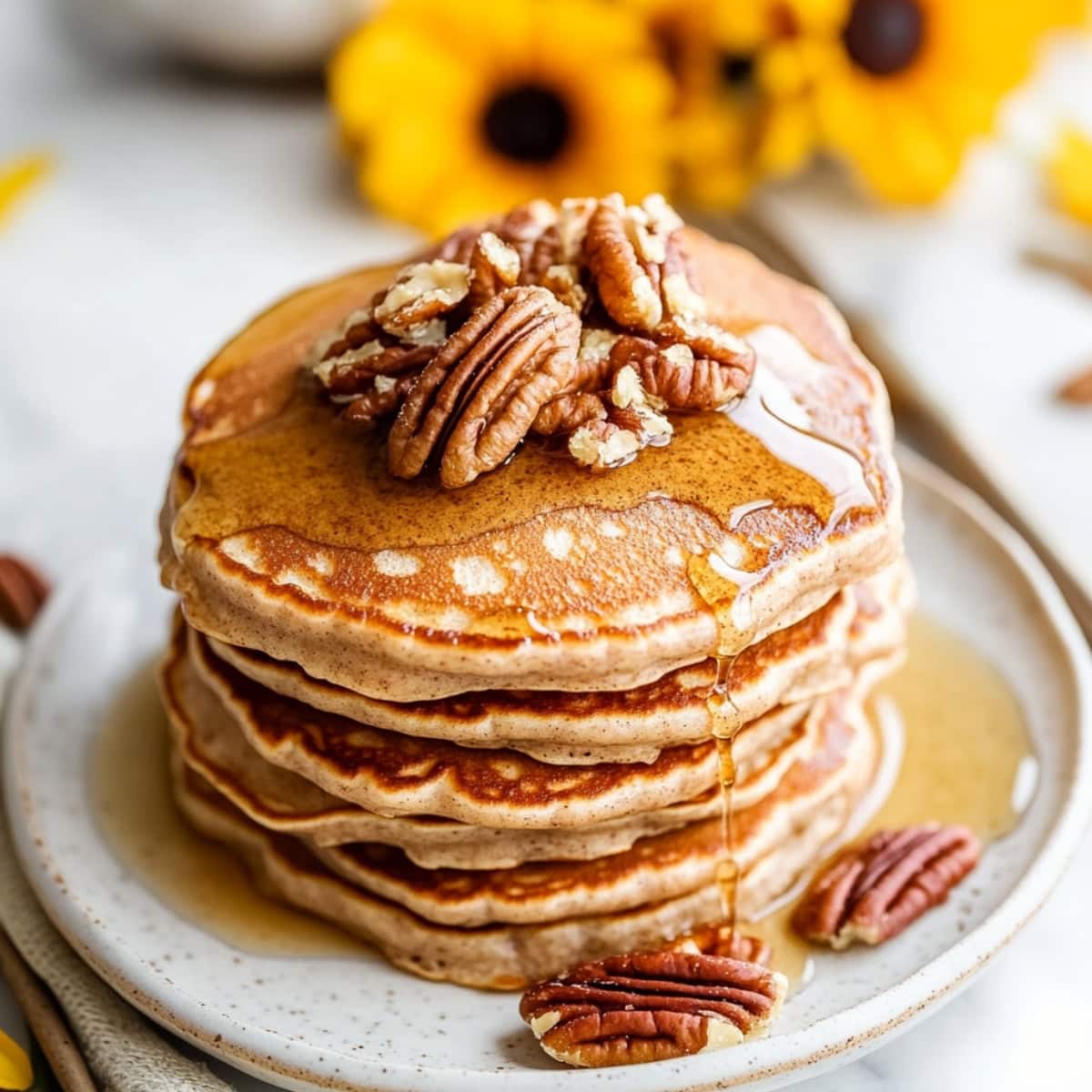 Close-up of golden-brown pancakes with crunchy pecans and a drizzle of maple syrup.