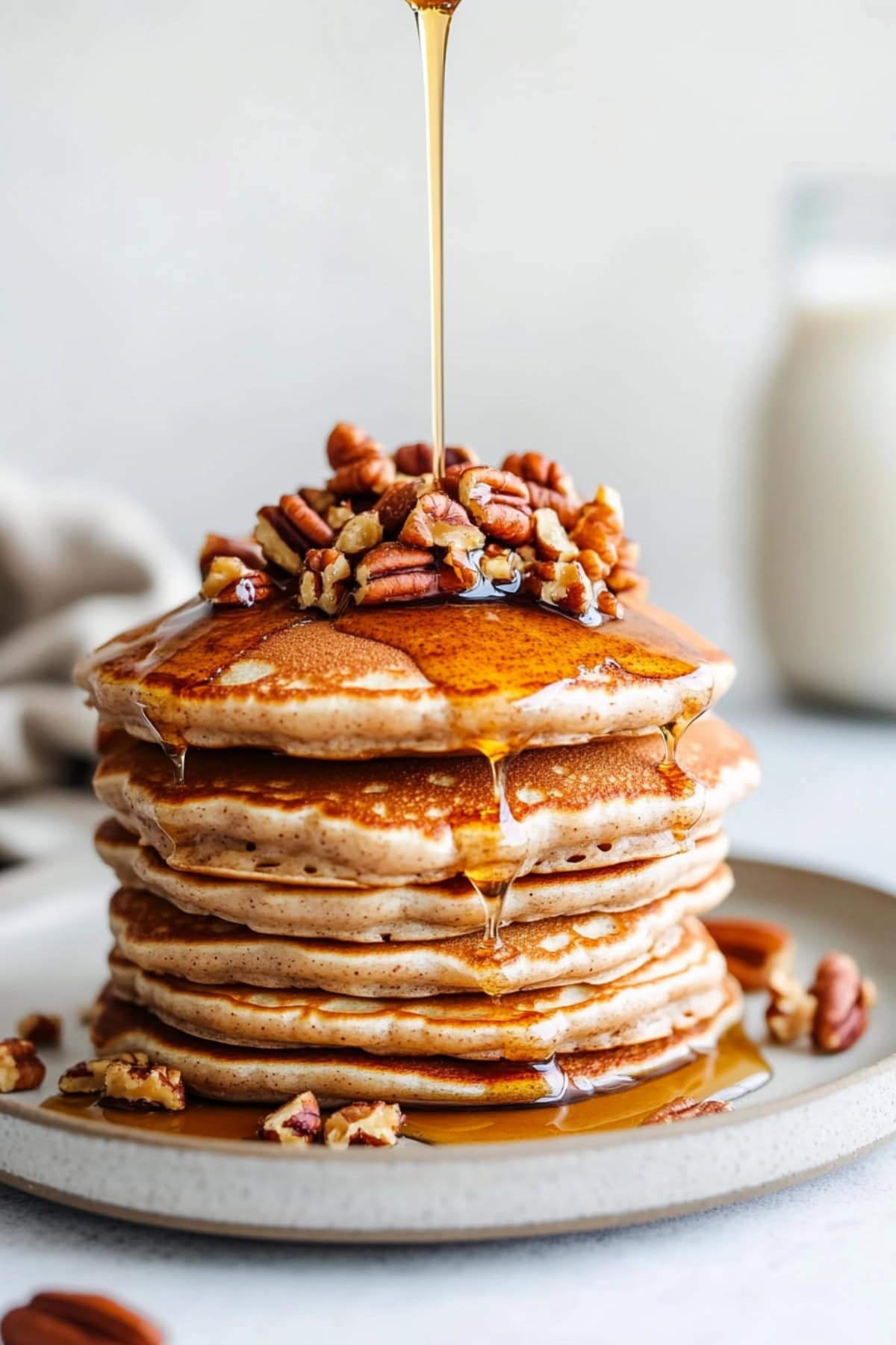 Pecan pancakes drizzled with maple syrup, stacked on a plate.