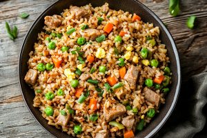 Bowl of homemade pork fried rice featuring green peas, carrots and scrambled eggs.