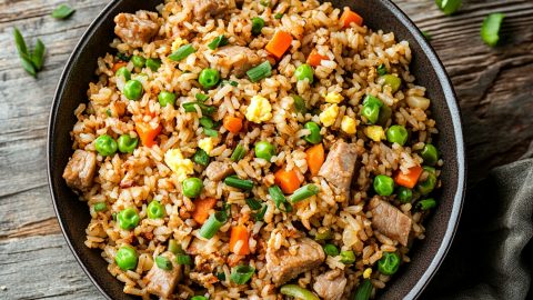 Bowl of homemade pork fried rice featuring green peas, carrots and scrambled eggs.