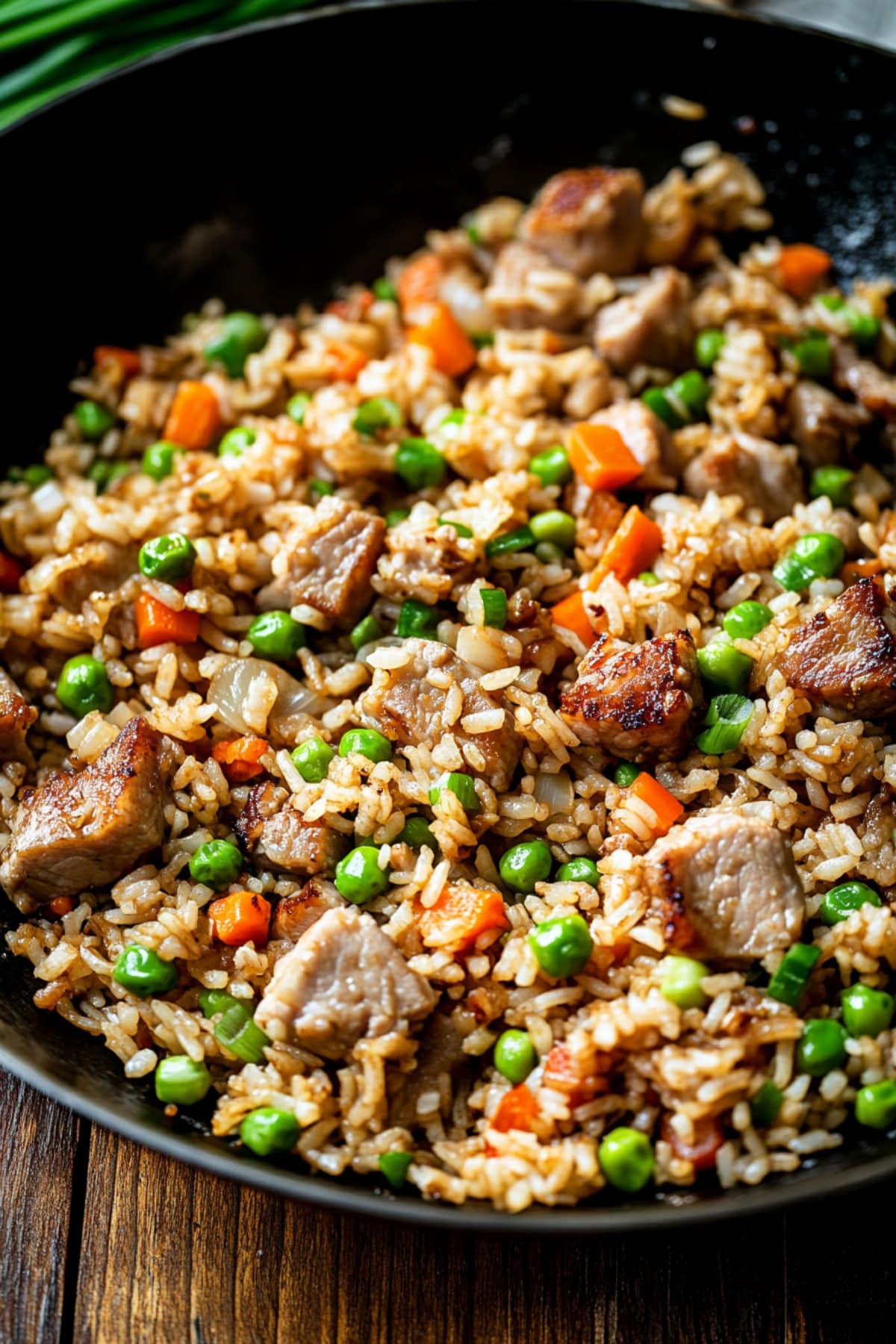 A close-up shot of pork friend rice with peas and carrots in a black skillet.