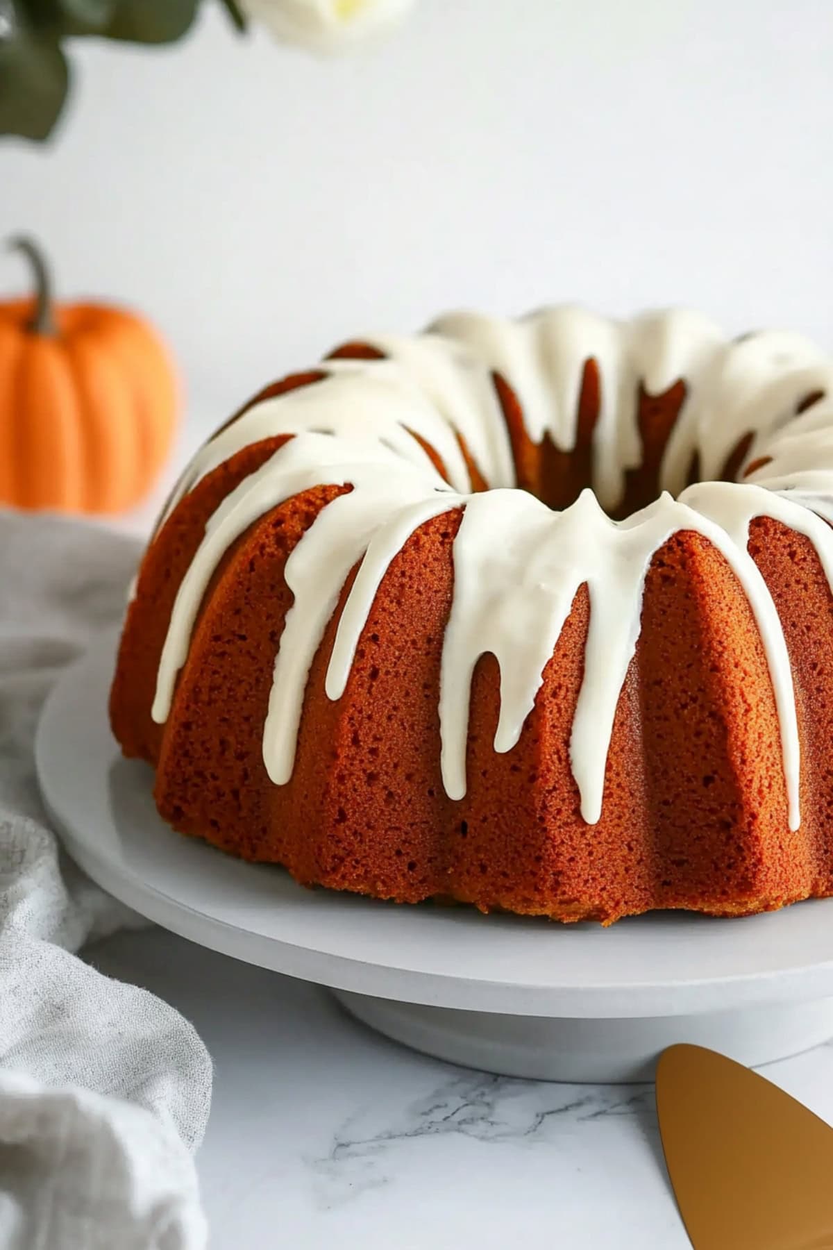 Whole pumpkin bundt cake drizzled with cream cheese glaze on a cake stand, side view