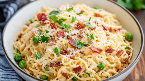 Ramen carbonara pasta garnished with chopped parsley, parmesan cheese and bacon served in a white bowl.