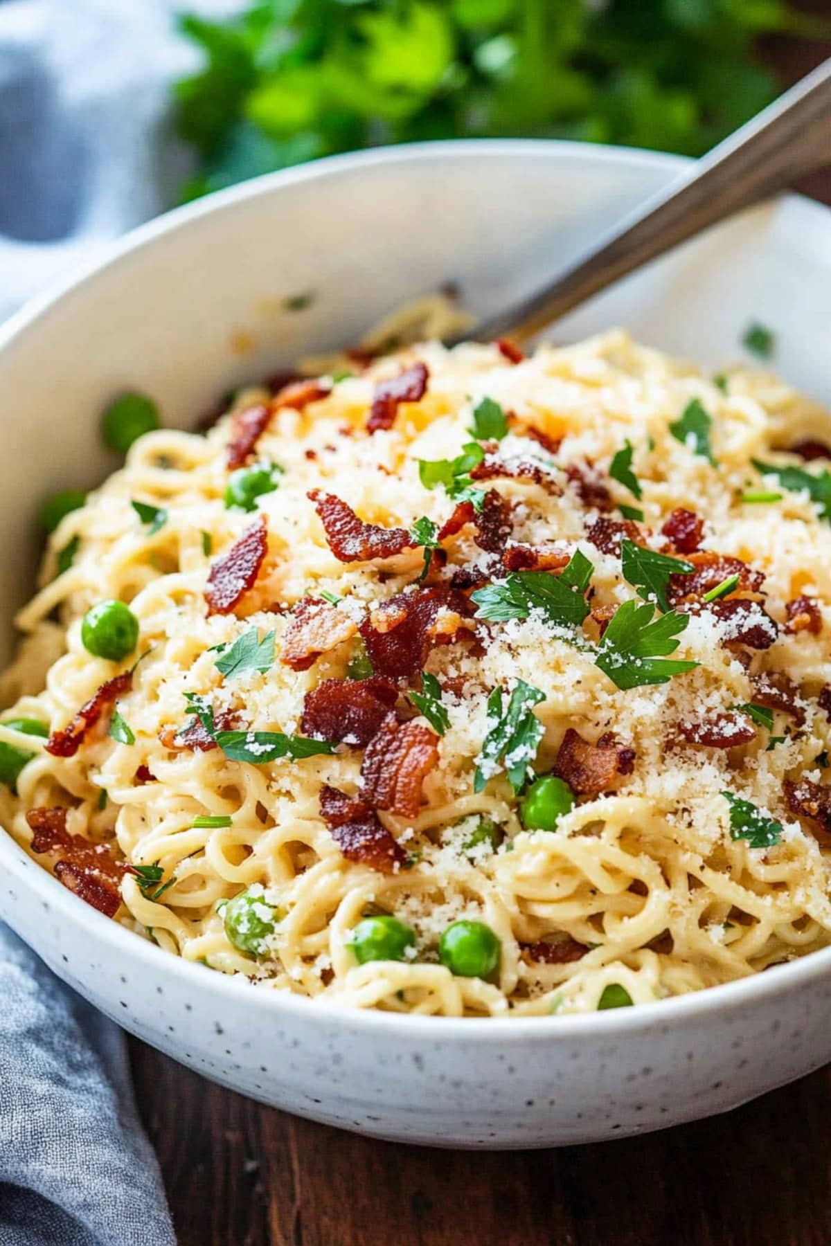 Ramen carbonara served in a white bowl garnished with bacon crumbles and chopped parsley.