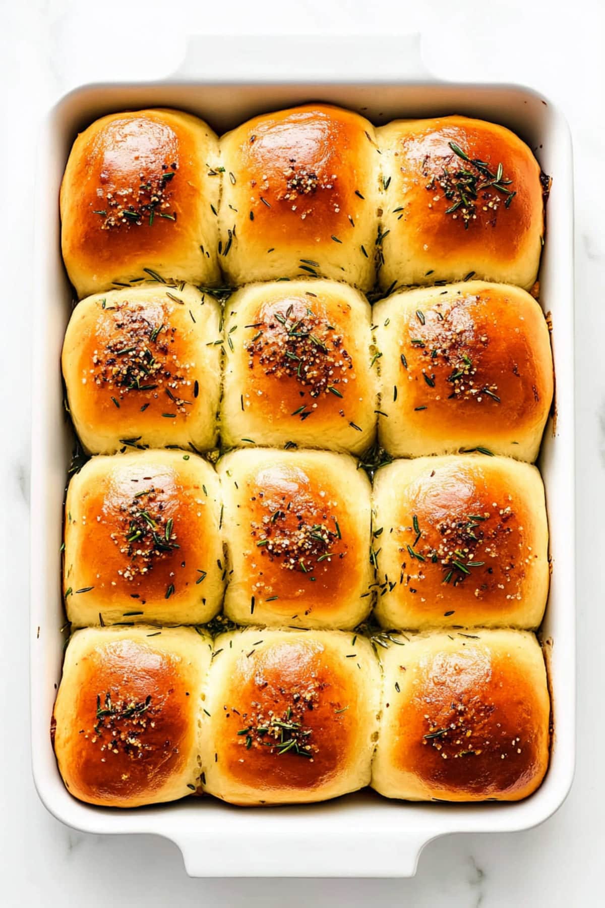 A white baking dish filled with rosemary dinner rolls, top view