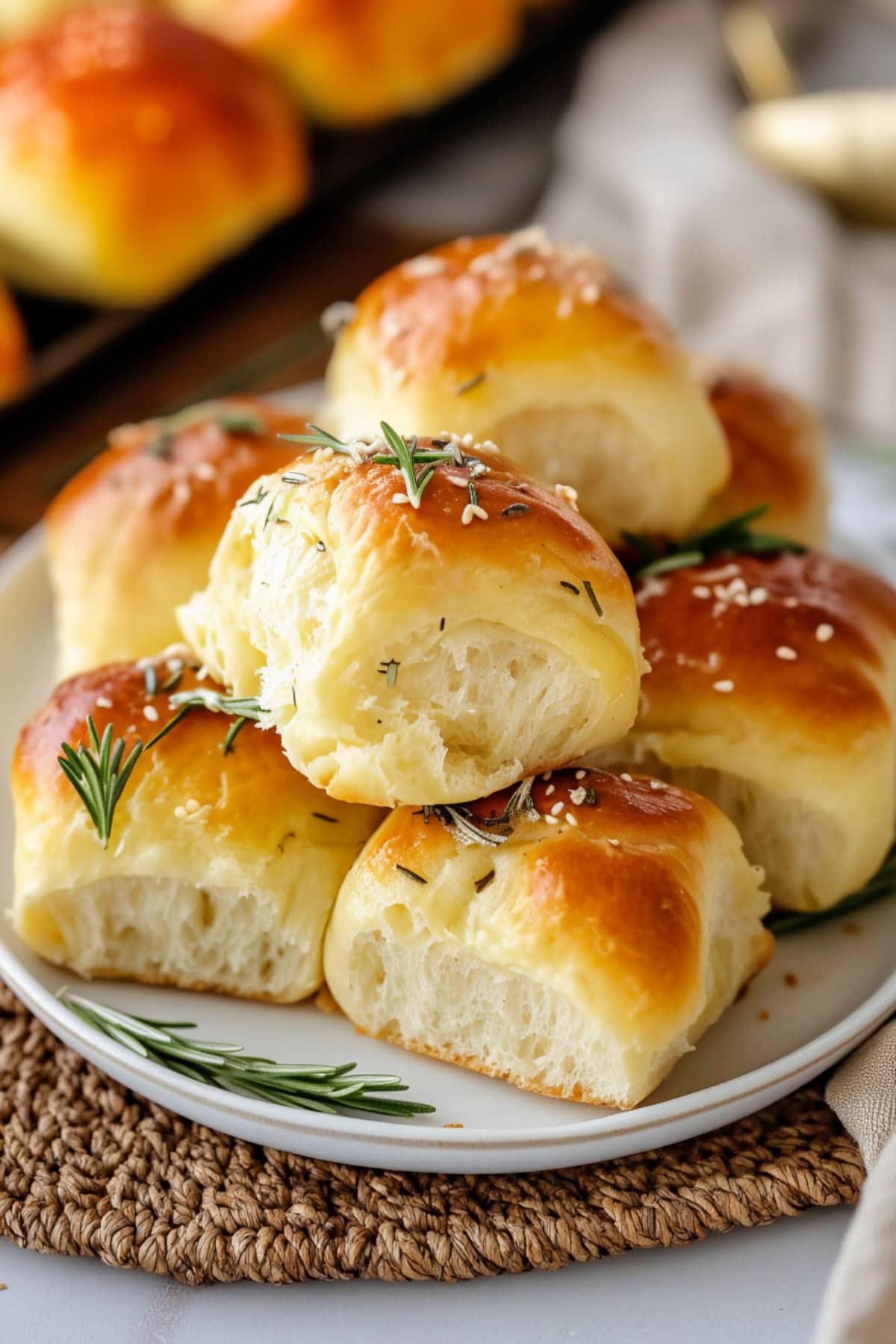 Soft and fluffy homemade rosemary dinner rolls stacked on a plate.