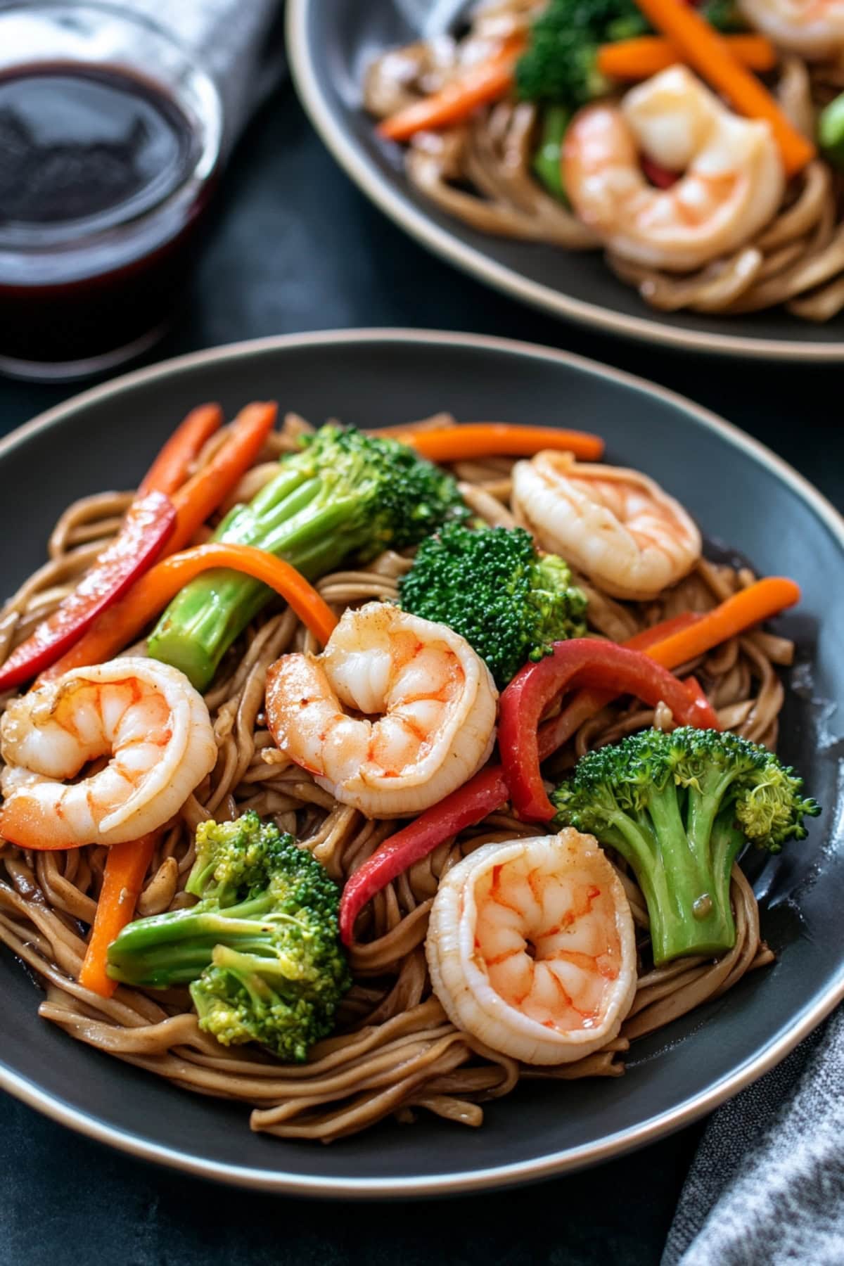 Plates of stir fry shrimps with noodles on a table.
