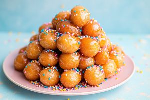 Struffoli arranged in a pyramid shape, the honey glistening and the sprinkles adding pops of color.