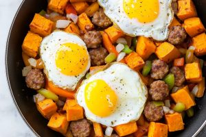 Close-up of sweet potato hash with crispy sausage pieces and perfectly cooked eggs with runny yolks.