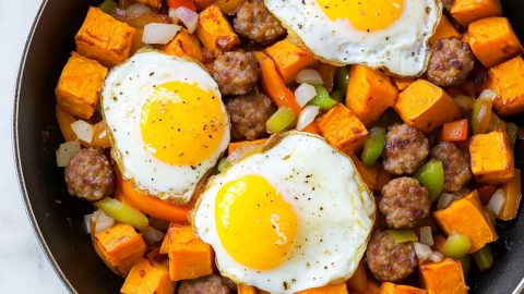 Close-up of sweet potato hash with crispy sausage pieces and perfectly cooked eggs with runny yolks.