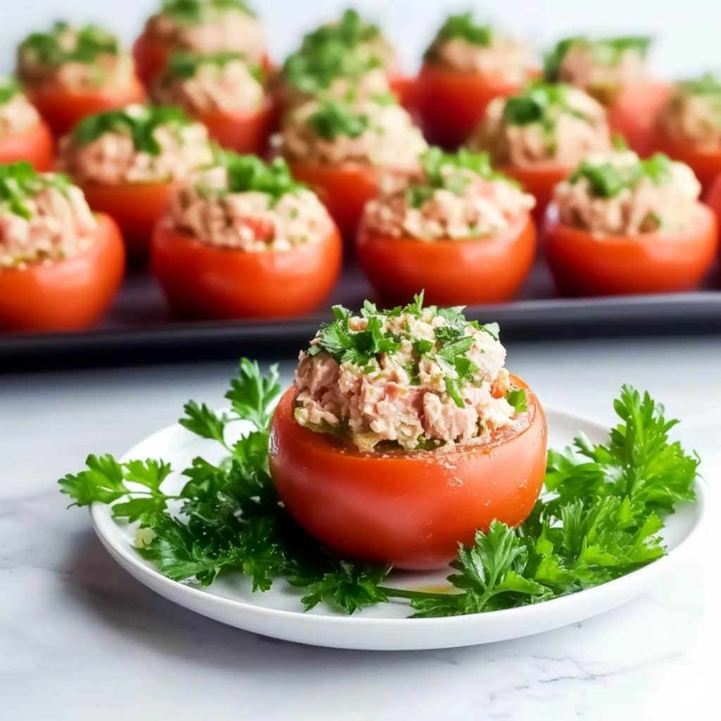 Tuna mixture stuffed tomatoes served in a white plate garnished with arugula leaves.