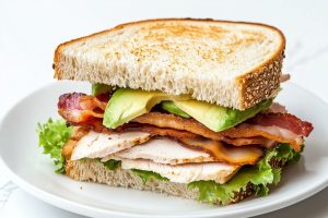 Sliced in half serving of turkey avocado sandwich served in a white plate.