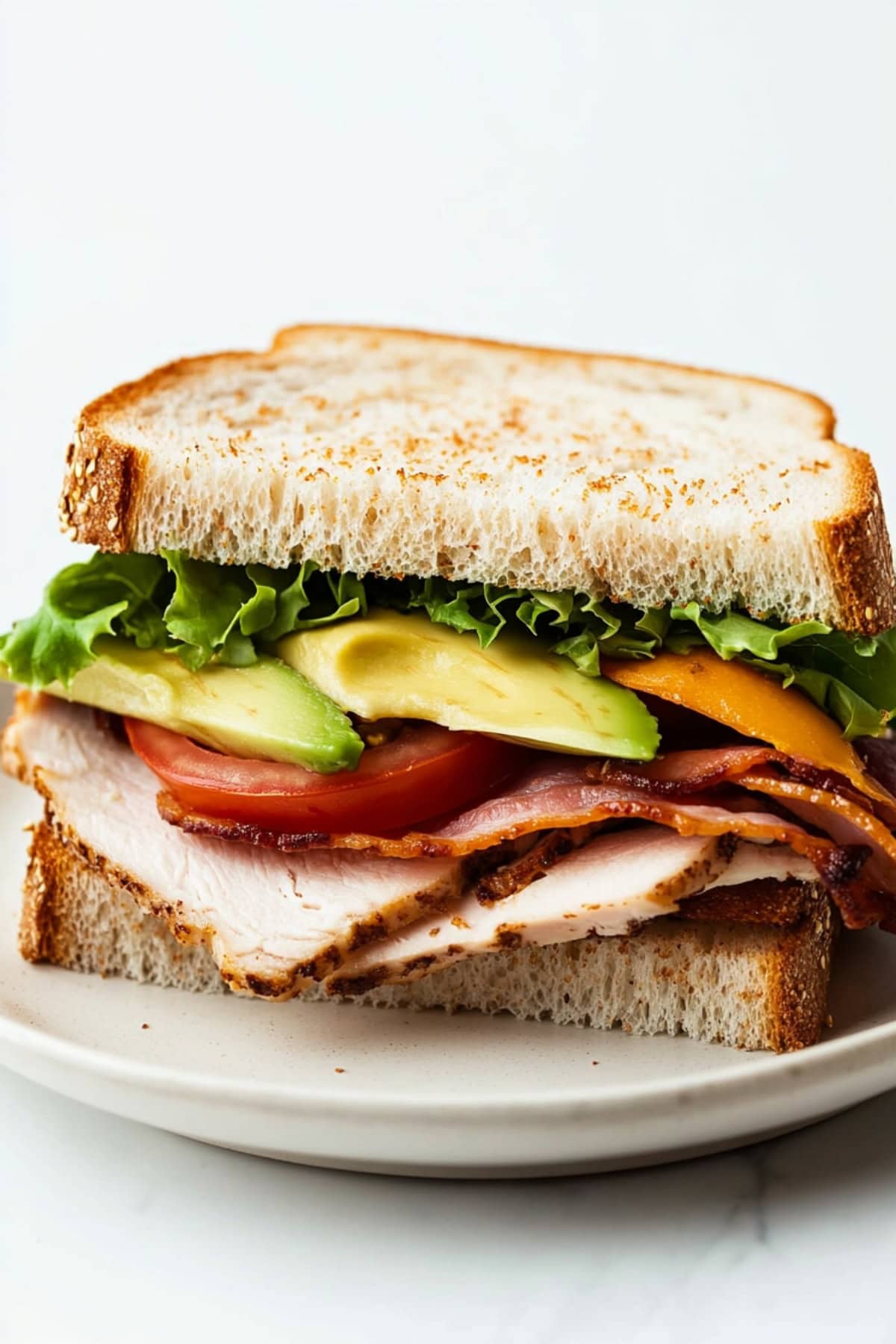 Sliced in half serving of turkey avocado sandwich served in a white plate.