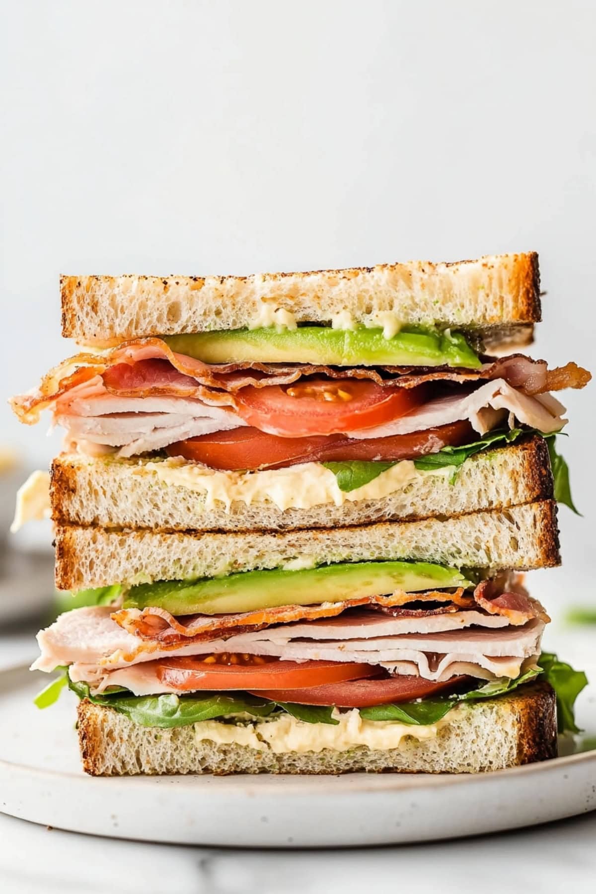 Sliced sandwich with turkey, avocado, tomatoes and lettuce inside served on a white plate.