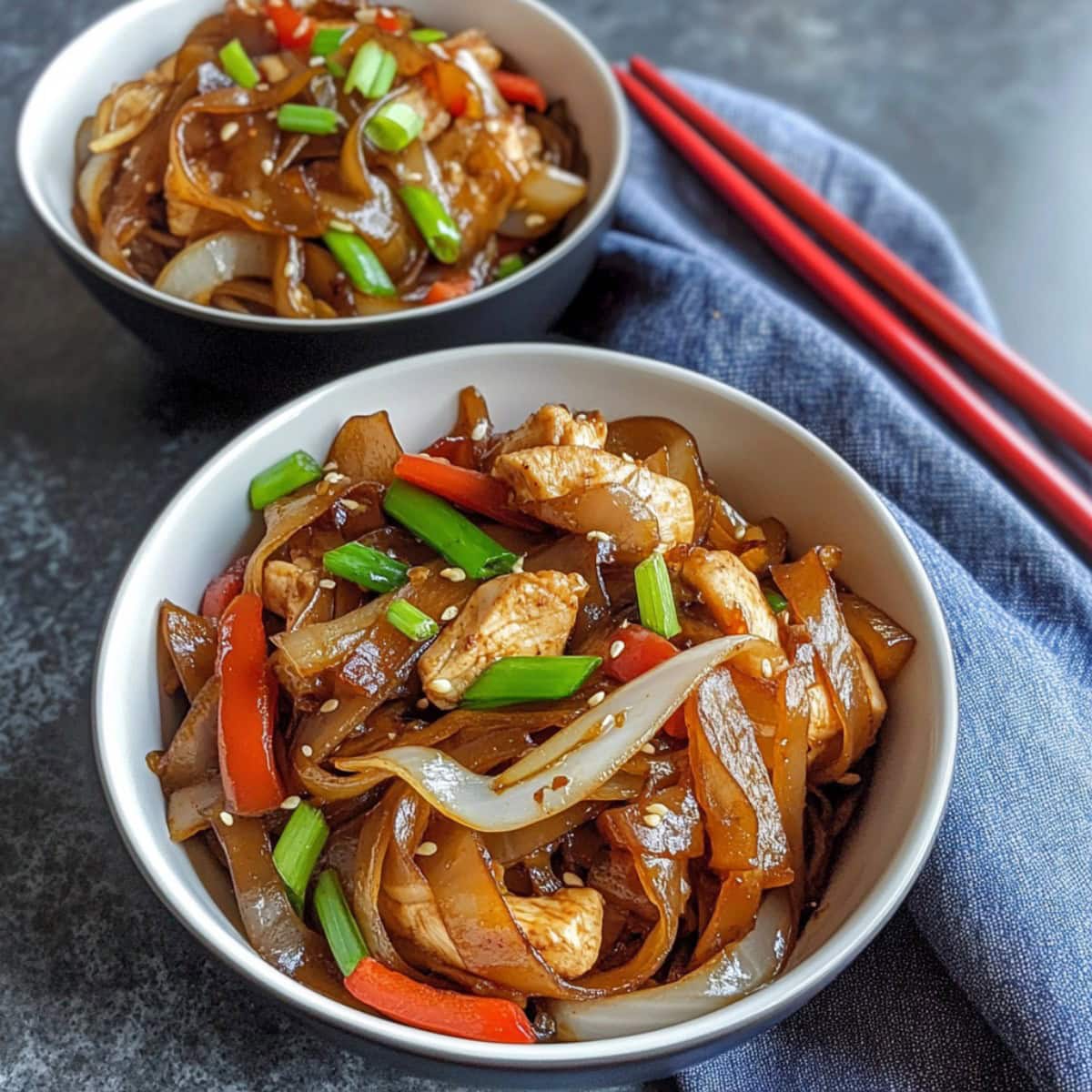 Two bowls of homemade chicken chow fun with green onions and bean sprouts.