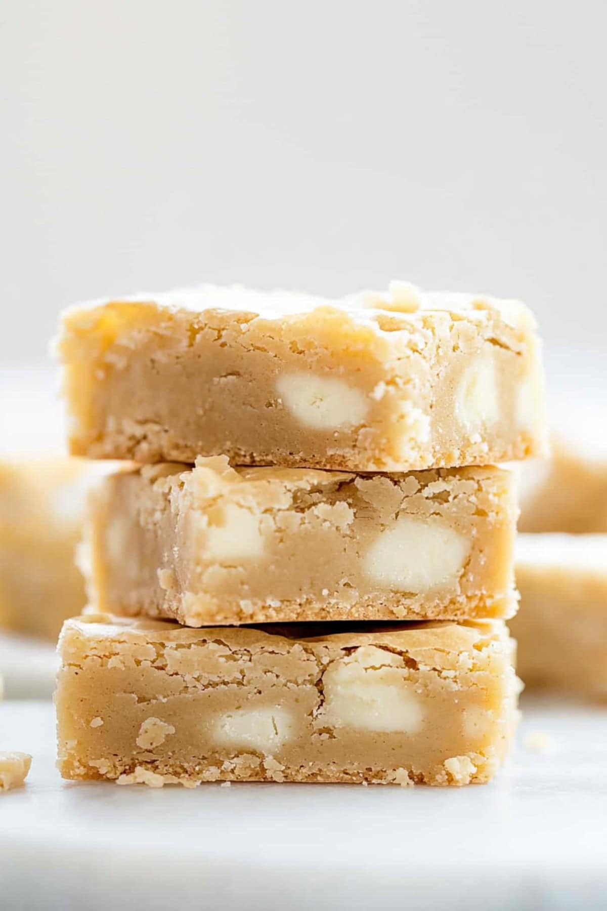 Three slices of white chocolate brownies stacked on top of each other sitting on a white marble table, side view, close up