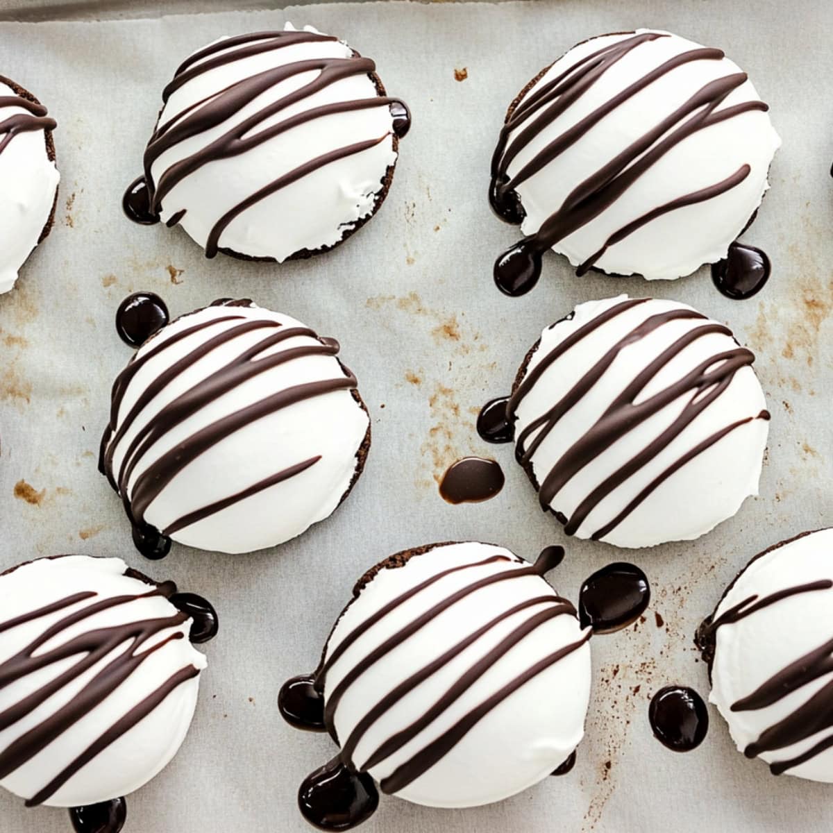 White chocolate covered oreos on parchment paper drizzle with dark chocolate, overhead view.