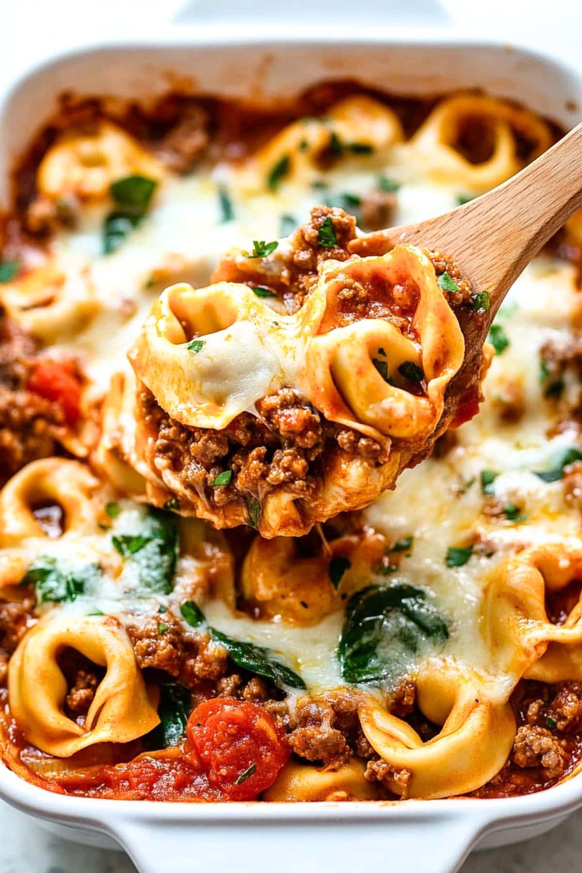 Baked tortellini pasta in a baking dish scooped with a wooden spoon.