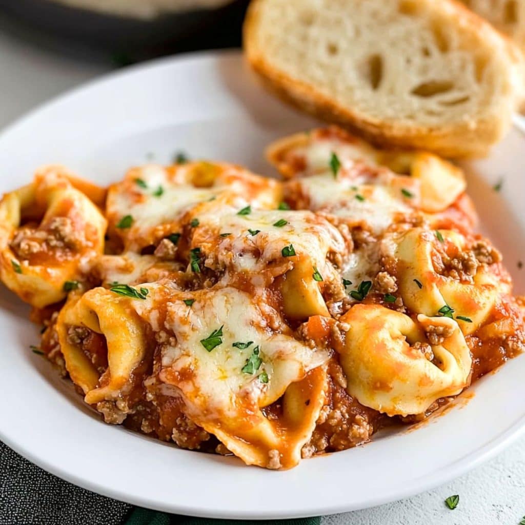 Serving of baked tortellini in a white plate with garlic bread.