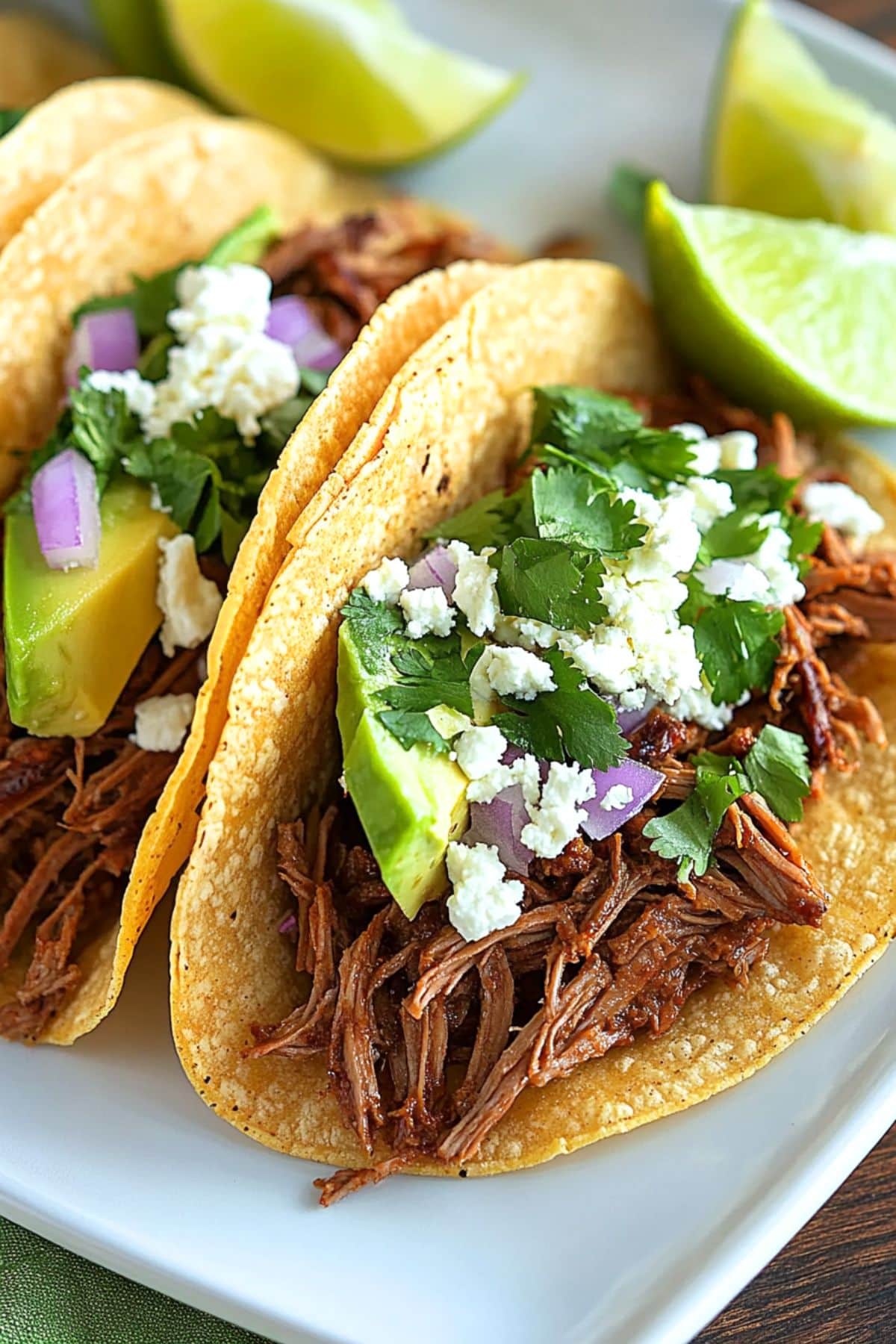 Shredded chuck roast served in a corn tortilla topped with crumbled cheese, chopped onions and parsley with lime garnish on the side.