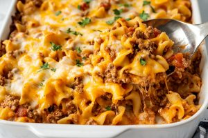 A casserole dish filled with beef noodle casserole, garnished with fresh parsley on top.