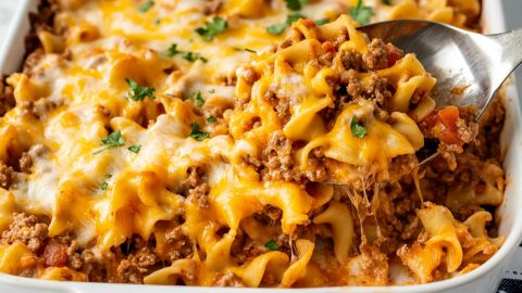 A casserole dish filled with beef noodle casserole, garnished with fresh parsley on top.
