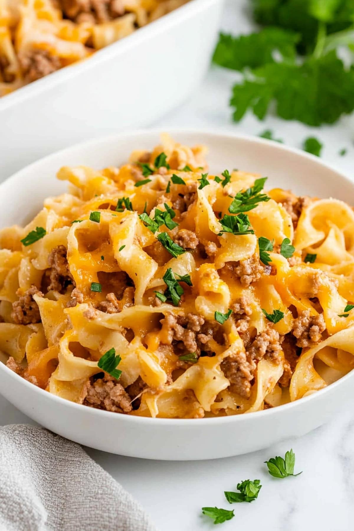 Ground beef and egg noodles in a bowl, with fresh herbs.