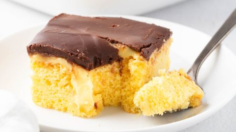Square slice of Boston cream pie poke cake, with a fork served in a white plate.