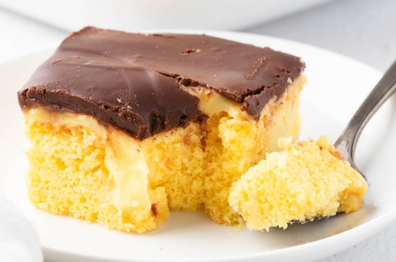 Square slice of Boston cream pie poke cake, with a fork served in a white plate.