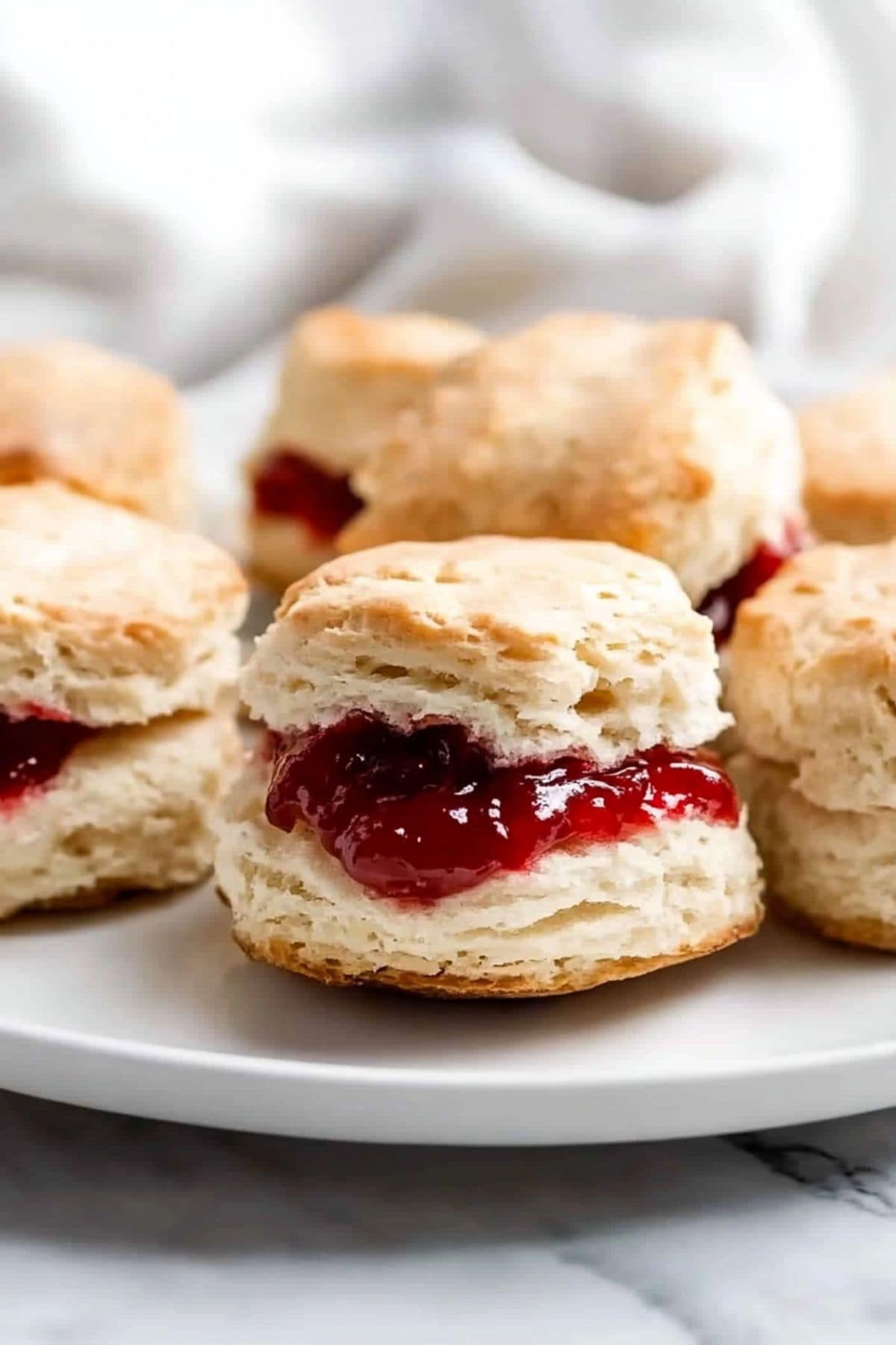 Buttermilk biscuits with strawberry jam arranged in a white plate.